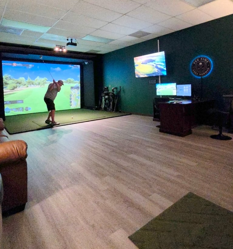 Person using indoor golf simulator in dark teal room with large projection screen and monitoring displays