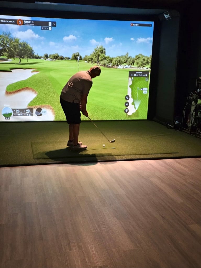 Person using indoor golf simulator, swinging club on mat with large screen displaying virtual golf course