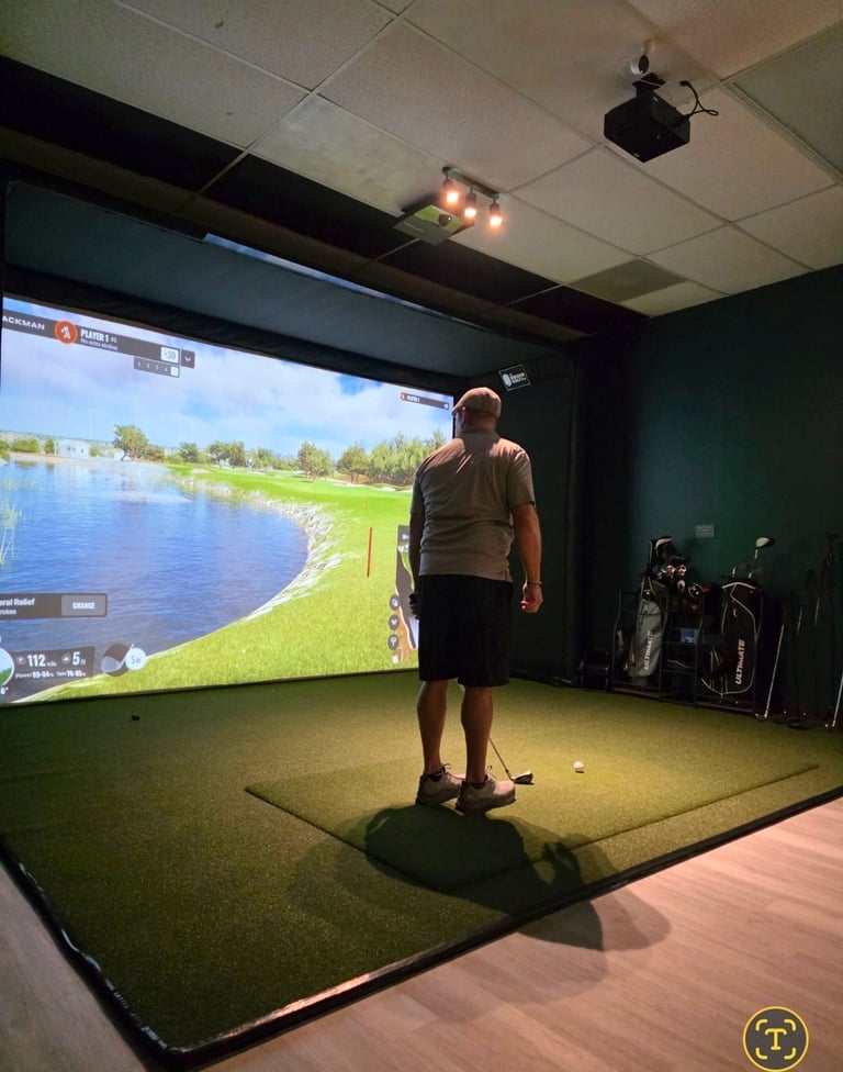 Man playing golf in an indoor simulator room with large screen display showing a golf course