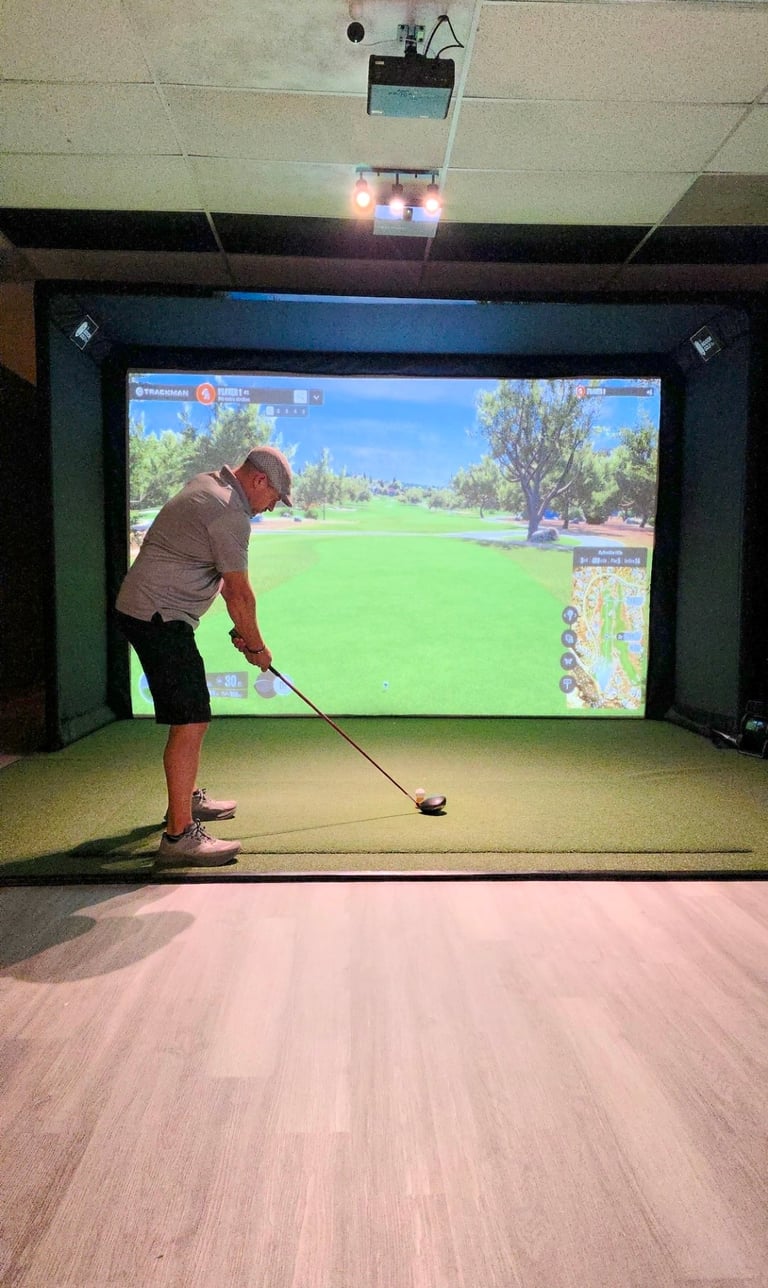Man using golf swing simulator indoors with large screen displaying virtual golf course and putting green