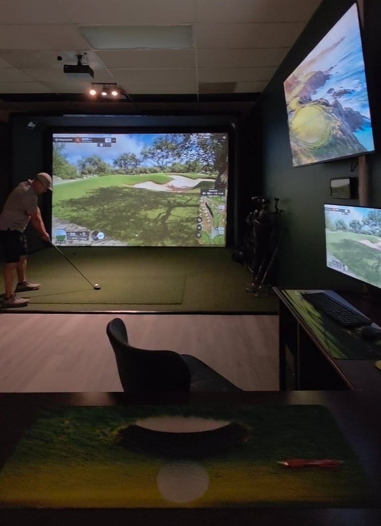 Indoor golf simulator setup with player at swing station, multiple screens displaying golf course and metrics, and projection display showing game interface